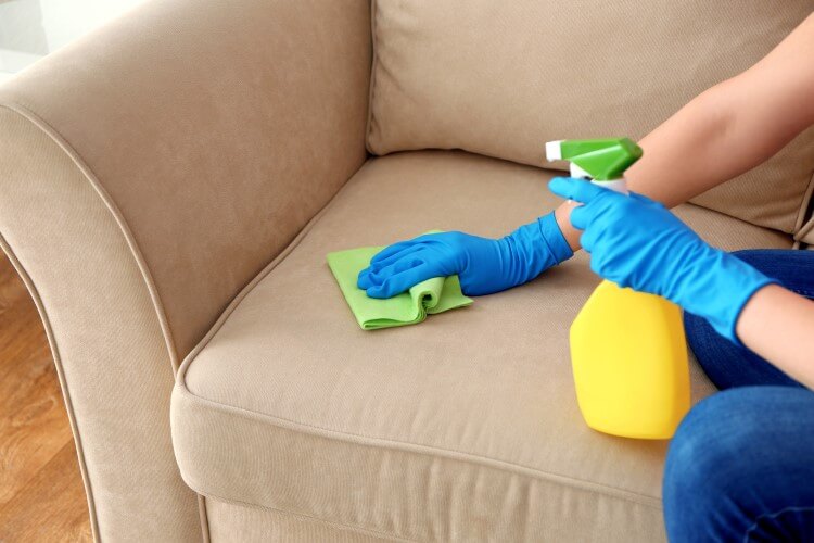 Pessoa limpando sofá de linho bege com pano e borrifador