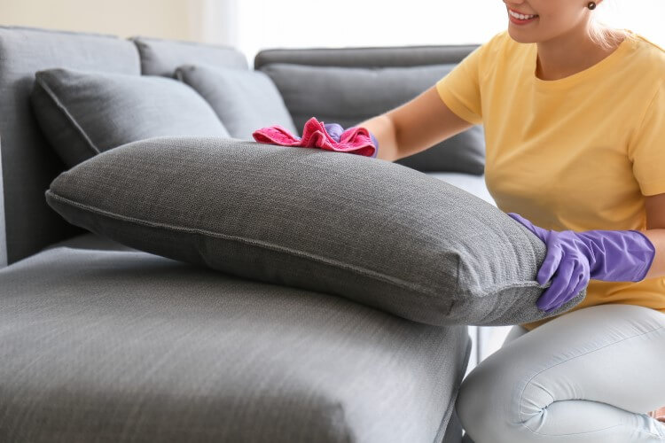 Mulher com pano limpando sofá de linho cinza
