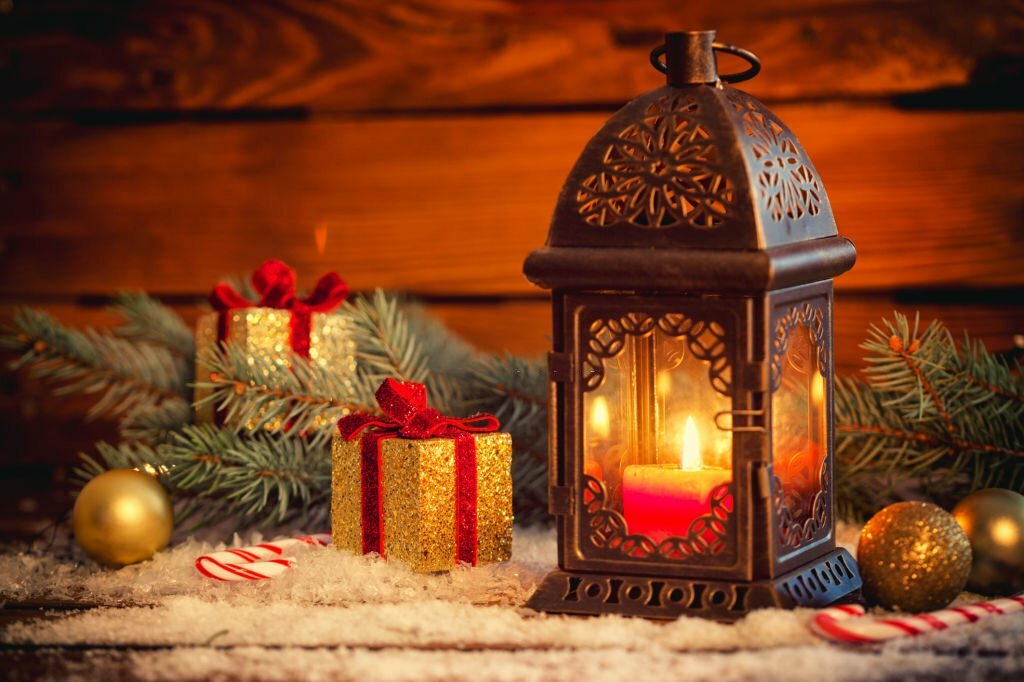 Decoração de natal com luminária de metal com vela, bolas douradas e caixas douradas com laços de fita vermelha.