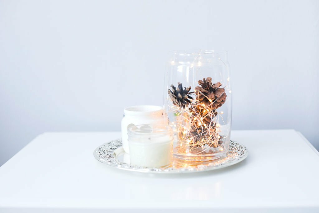 Bandeja com velas e pote de vidro decorado com pinhas e cordão transparente com luzes de LED.