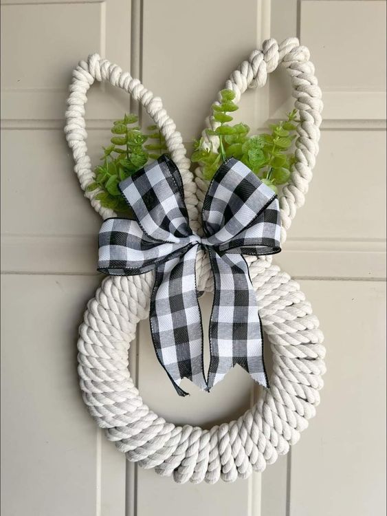 guirlanda decorativa feita com cordão branco, folhas verdes e laço de fita xadrez preto e branco.