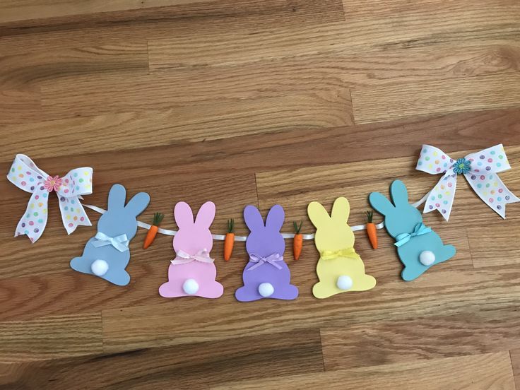 Varal de coelhos de páscoa feitos de papel colorido enfeitados com cenouras de pelúcia e laços.