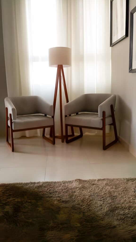 Sala decorada com cores neutras, duas poltronas, luminária com bsase de madeira, cortinas e tapete.