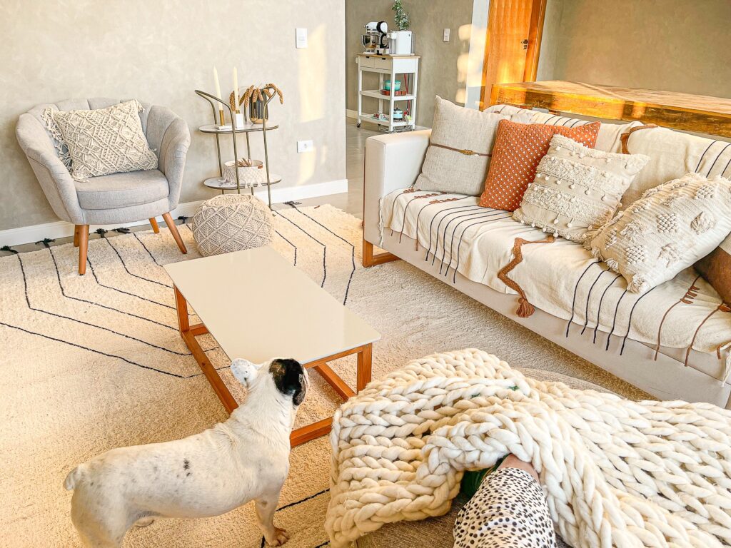 Sala decorada com diversos elementos feitos de lã e crochê, sofá, poltrona e mesa de centro com base de madeira. Tudo de acordo com o estilo boho. Cachorro Bullgod Francês na sala.