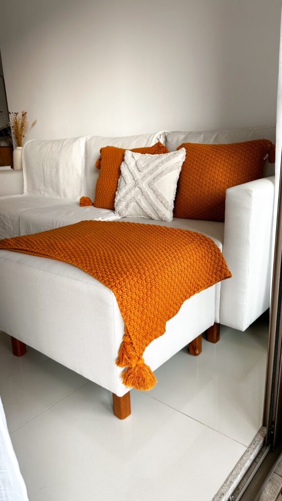 Sofá em cor neutra decorado com almofadas texturizadas e manta de lã na cor terracota criam o efeito de contraste na decoração Boho.