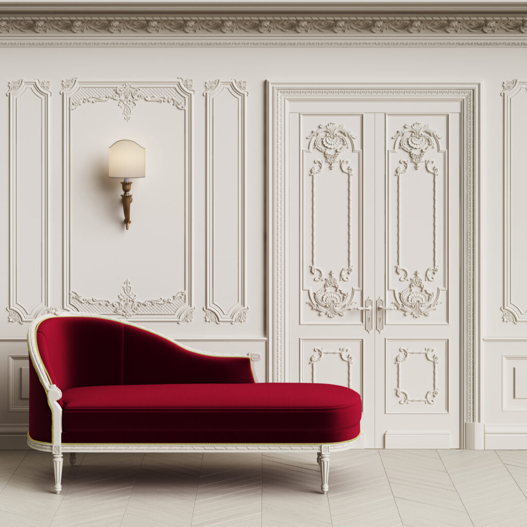 Chaise vermelha de veludo em sala com elementos clássicos aplicados na parede branca. 